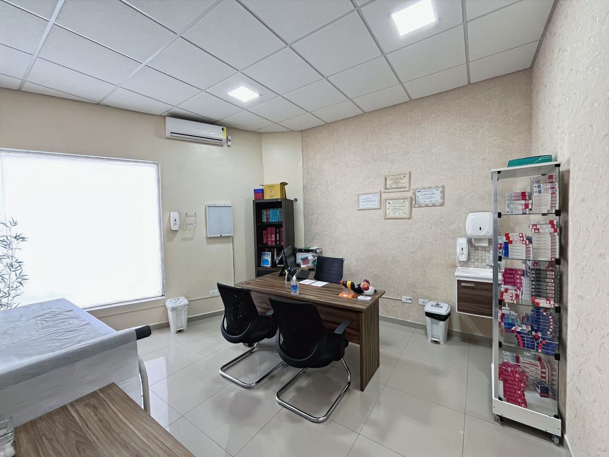 Consultório médico com mesa de atendimento, cadeiras e maca de exame