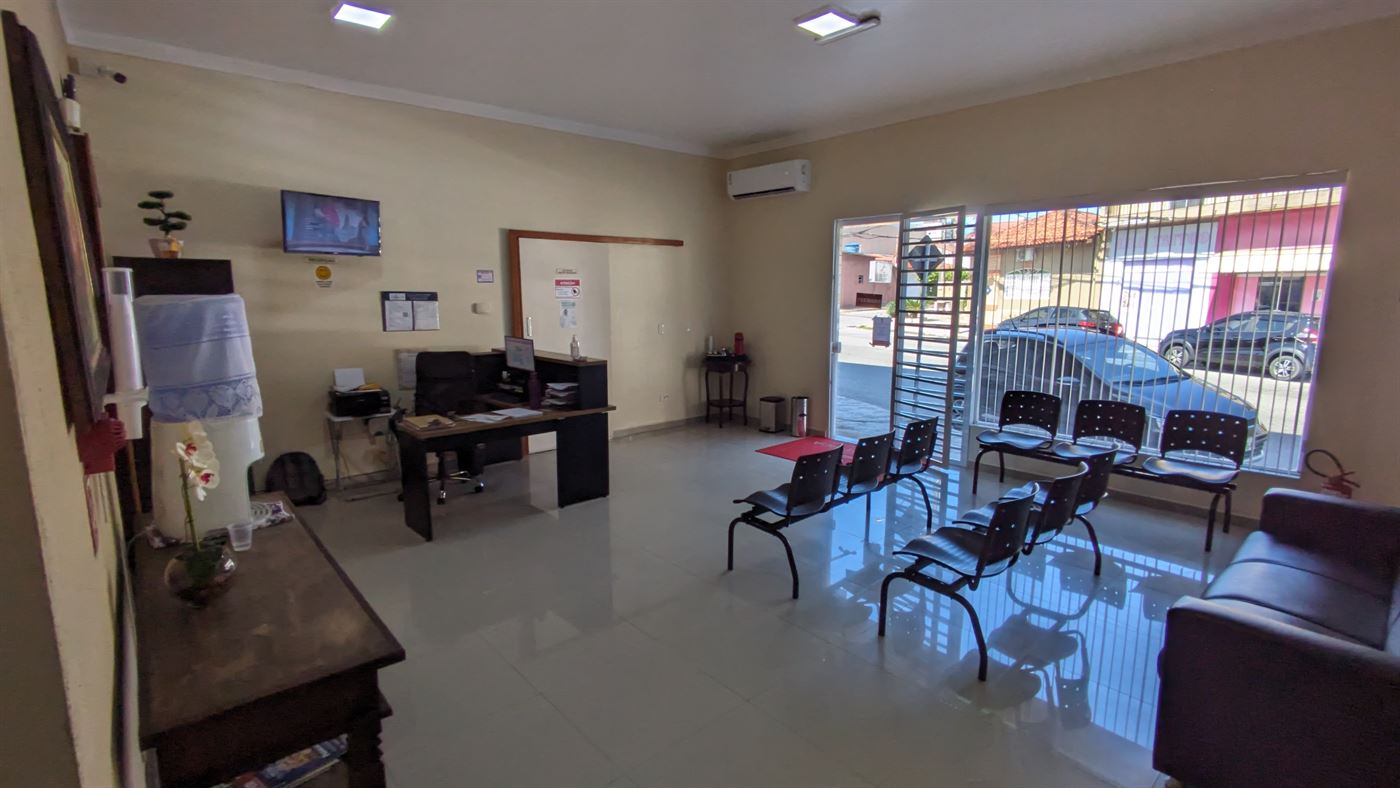 Área de recepção com mesa de atendimento, cadeiras de espera e porta de vidro para a rua